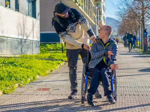 Ein Bild eines Menschen mit Behinderung, der mit einem Menschen an einem sonnigen Tag spaziert.