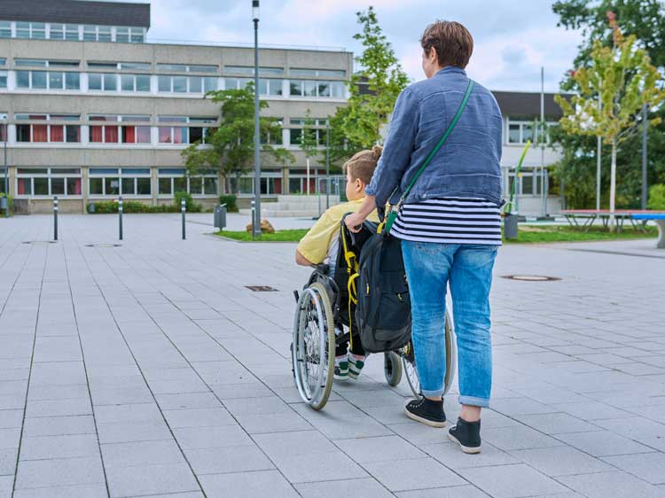 Ein Bild eines Menschen mit Behinderung, der mit einem Menschen an einem sonnigen Tag spaziert.
